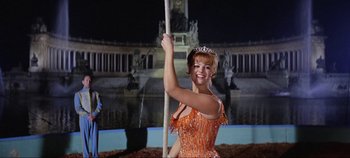Movie still from “Circus World” (1964), directed by Henry Hathaway – A woman in an orange dress holding onto a pole; Medium shot, Low angle