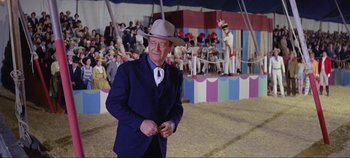 Movie still from “Circus World” (1964), directed by Henry Hathaway – A man in a suit and hat standing in front of an audience; Medium shot, Low angle