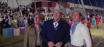 Movie still from “Circus World” (1964), directed by Henry Hathaway – A group of men standing next to each other in front of a crowd of onlookers; Medium shot, Low angle