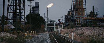 Movie still from “The Day the Earth Stood Still” (2008), directed by Scott Derrickson – A train track with a train on the tracks and a gas flare in the background; Extreme Wide shot, High angle
