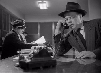 Movie still from “City That Never Sleeps” (1953), directed by John H. Auer – A man sitting at a table talking on a phone; Medium shot, Low angle
