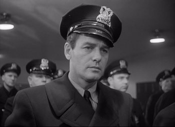 Movie still from “City That Never Sleeps” (1953), directed by John H. Auer – Black and white photograph of a man in a police uniform; Close Up shot, Low angle