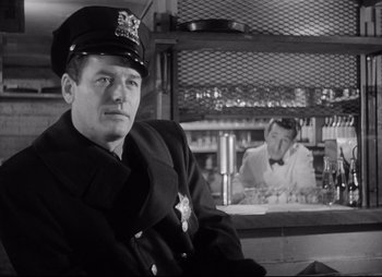 Movie still from “City That Never Sleeps” (1953), directed by John H. Auer – A police officer sitting in front of a counter; Medium shot, Over the shoulder angle