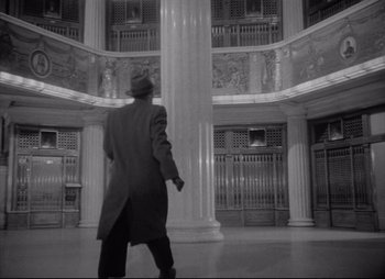 Movie still from “City That Never Sleeps” (1953), directed by John H. Auer – A man in a coat walking in a large room; Wide shot, Low angle