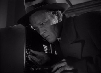 Movie still from “City That Never Sleeps” (1953), directed by John H. Auer – An older man in a hat and a suit looking down at a keyboard; Close Up shot, Low angle