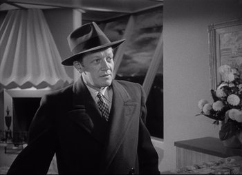 Movie still from “City That Never Sleeps” (1953), directed by John H. Auer – A man in a suit and hat standing in front of a mirror; Medium shot, Low angle