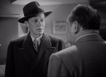 Movie still from “City That Never Sleeps” (1953), directed by John H. Auer – A man wearing a suit and hat talking to another man in a suit; Medium shot, Over the shoulder angle