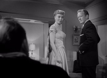 Movie still from “City That Never Sleeps” (1953), directed by John H. Auer – A man and a woman standing next to each other in a room; Medium shot, Over the shoulder angle