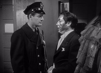 Movie still from “City That Never Sleeps” (1953), directed by John H. Auer – Two men in uniforms are standing next to each other; Medium shot, Over the shoulder angle