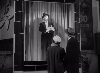Movie still from “City That Never Sleeps” (1953), directed by John H. Auer – A man in a suit and hat standing in front of two other men; Wide shot, Low angle