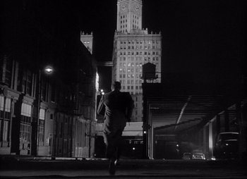 Movie still from “City That Never Sleeps” (1953), directed by John H. Auer – A black and white photo of a man in a suit running down the street; Wide shot, Low angle