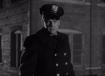 Movie still from “City That Never Sleeps” (1953), directed by John H. Auer – A man wearing a uniform and a hat standing in front of a brick building; Medium shot, Low angle