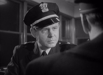 Movie still from “City That Never Sleeps” (1953), directed by John H. Auer – An old black and white photo of a man in a police uniform; Close Up shot, Over the shoulder angle