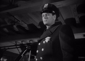Movie still from “City That Never Sleeps” (1953), directed by John H. Auer – A black and white photo of a man in a police uniform; Close Up shot, Low angle