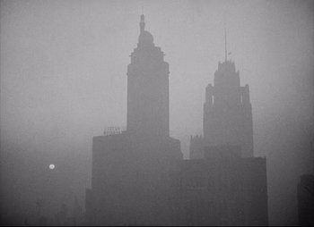Movie still from “City That Never Sleeps” (1953), directed by John H. Auer – A black and white photo of two buildings in the fog; Extreme Wide shot, Low angle