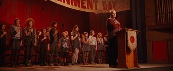Movie still from “City of Ember” (2008), directed by Gil Kenan – A group of people standing on a stage with a man at a podium; Wide shot, Low angle