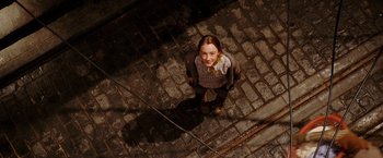 Movie still from “City of Ember” (2008), directed by Gil Kenan – A young girl standing on a brick walkway; Wide shot, Overhead angle