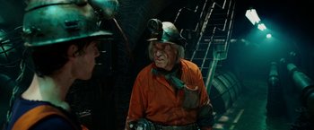 Movie still from “City of Ember” (2008), directed by Gil Kenan – An older man in an orange shirt wearing a green hat; Medium shot, Over the shoulder angle