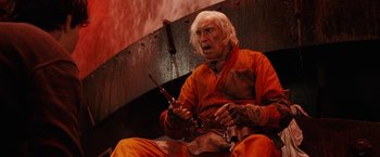 Movie still from “City of Ember” (2008), directed by Gil Kenan – An old man in an orange outfit holding a pair of sticks; Medium shot, Low angle