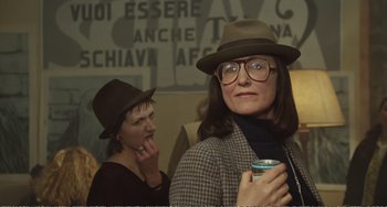 Movie still from “City of Women” (1980), directed by Federico Fellini – A woman wearing a hat and glasses while holding a drink; Close Up shot, Over the shoulder angle