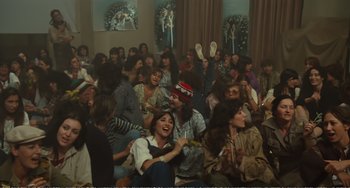 Movie still from “City of Women” (1980), directed by Federico Fellini – A group of people sitting and standing in a room; Wide shot, High angle