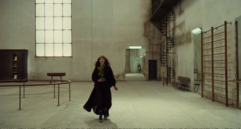 Movie still from “City of Women” (1980), directed by Federico Fellini – A woman is walking in a room with stairs; Wide shot, Low angle