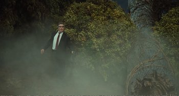 Movie still from “City of Women” (1980), directed by Federico Fellini – A man in a suit and tie standing next to a tree; Wide shot, Low angle