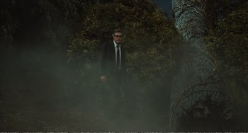 Movie still from “City of Women” (1980), directed by Federico Fellini – A man in a suit and tie standing next to a tree; Wide shot, Low angle
