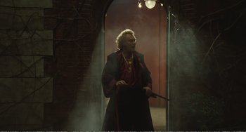 Movie still from “City of Women” (1980), directed by Federico Fellini – An older woman is holding a wand in a doorway; Wide shot, Low angle