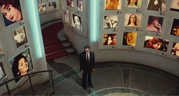 Movie still from “City of Women” (1980), directed by Federico Fellini – A man in a suit standing in front of a wall of pictures; Wide shot, High angle