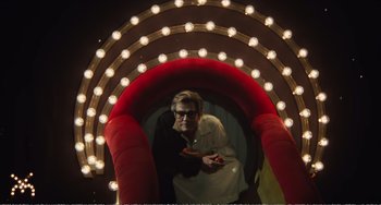 Movie still from “City of Women” (1980), directed by Federico Fellini – A man standing inside of an arch with lights around it; Wide shot, Low angle