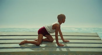 Movie still from “City of Women” (1980), directed by Federico Fellini – A young boy sitting on the ground on top of a platform; Wide shot, High angle