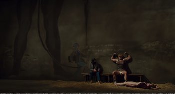 Movie still from “City of Women” (1980), directed by Federico Fellini – Two men sit on a bench in front of a painting; Wide shot, Low angle