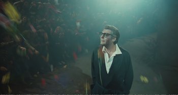 Movie still from “City of Women” (1980), directed by Federico Fellini – A man in a black suit and white shirt is standing in front of a group of people; Medium shot, Low angle