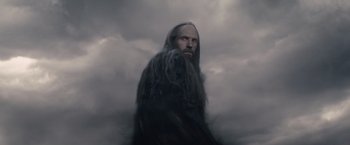 Movie still from “Clash of the Titans” (2010), directed by Louis Leterrier – A man with long hair and a beard standing in the middle of a cloud filled sky; Medium shot, Low angle