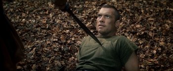 Movie still from “Clash of the Titans” (2010), directed by Louis Leterrier – A man laying in the leaves holding an axe; Close Up shot, High angle