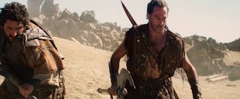 Movie still from “Clash of the Titans” (2010), directed by Louis Leterrier – A man with a sword and a knife walking in the desert; Medium shot, Over the shoulder angle