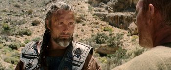 Movie still from “Clash of the Titans” (2010), directed by Louis Leterrier – A man with long hair and a beard is wearing a leather vest; Close Up shot, Over the shoulder angle