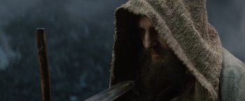 Movie still from “Clash of the Titans” (2010), directed by Louis Leterrier – A man with a long beard wearing a hood and holding a sword; Close Up shot, Over the shoulder angle