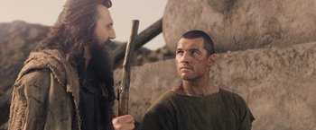 Movie still from “Clash of the Titans” (2010), directed by Louis Leterrier – A man holding a wooden stick in front of a bearded man; Close Up shot, Over the shoulder angle