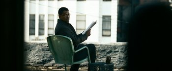 Movie still from “Cleaner” (2007), directed by Renny Harlin – A man sitting in a chair reading a book; Medium shot, Over the shoulder angle