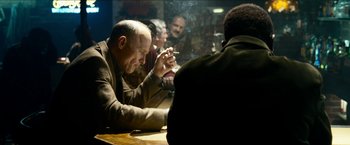 Movie still from “Cleaner” (2007), directed by Renny Harlin – A man smoking a cigarette while sitting at a table with other people; Medium shot, Over the shoulder angle