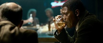 Movie still from “Cleaner” (2007), directed by Renny Harlin – A man drinking from a glass in front of a group of people; Close Up shot, Over the shoulder angle