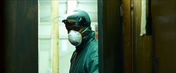Movie still from “Cleaner” (2007), directed by Renny Harlin – A man wearing a surgical mask in a room; Medium shot, Low angle