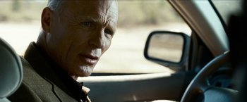 Movie still from “Cleaner” (2007), directed by Renny Harlin – An older man sitting in the driver's seat of a car; Close Up shot, Over the shoulder angle