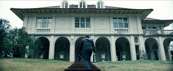 Movie still from “Cleaner” (2007), directed by Renny Harlin – A man walking up a set of stairs in front of a building; Extreme Wide shot, Low angle