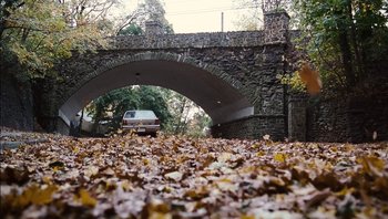 Movie still from “Clerks II” (2006), directed by Kevin Smith – A car is driving under a bridge in the fall leaves; Extreme Wide shot, High angle