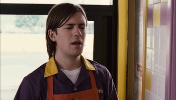 Movie still from “Clerks II” (2006), directed by Kevin Smith – A man in an orange and purple apron is standing in front of a window; Close Up shot, Low angle