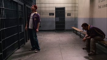 Movie still from “Clerks II” (2006), directed by Kevin Smith – A man standing next to a bench in a jail cell; Wide shot, High angle