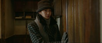 Movie still from “Cliff Walkers” (2021), directed by Yimou Zhang – A woman in a hat and gloves standing in front of a cabinet; Medium shot, Over the shoulder angle
